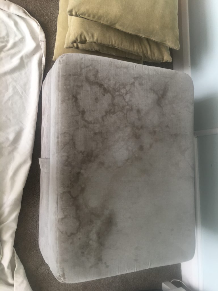 Fabric footstool with visible stains and discolouration before cleaning